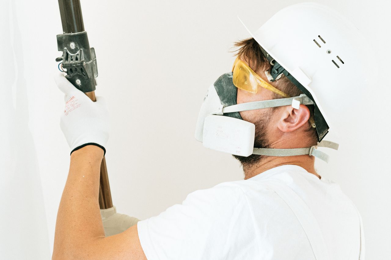 Construction worker wearing safety gear applying paint with a roller indoors. Focus on safety measures.