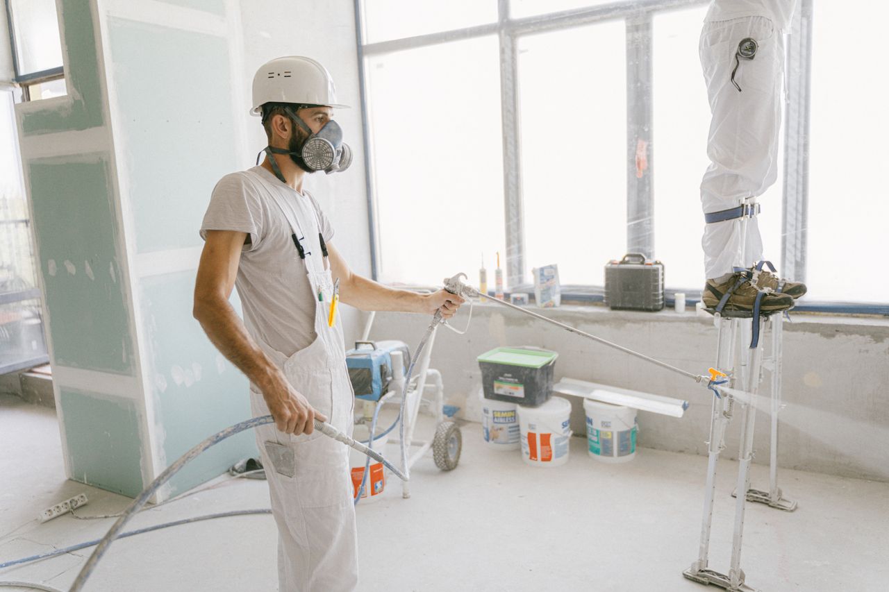 services-04 Two construction workers wearing protective gear and painting interior walls for a renovation project.