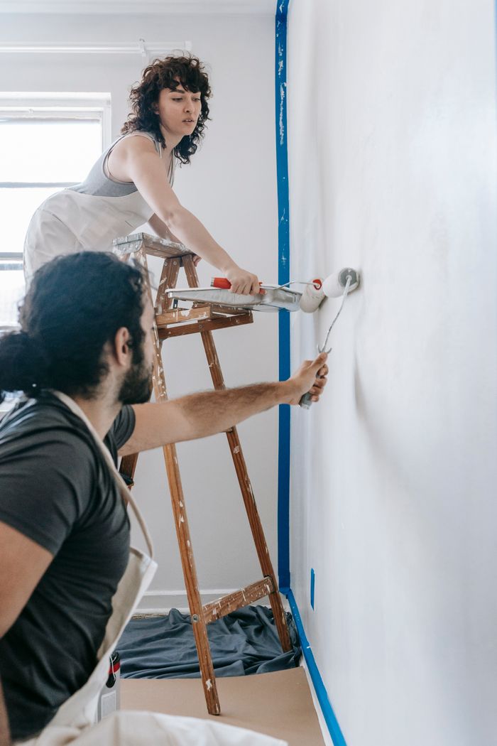 Couple renovating their home by painting a white wall together with rollers.