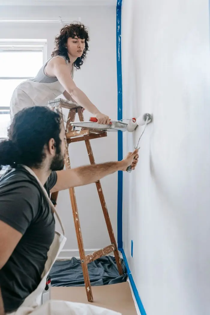 Couple renovating their home by painting a white wall together with rollers.