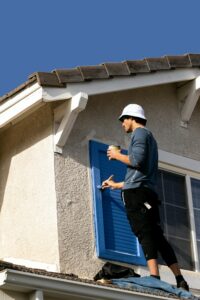 House painter applying blue paint to exterior shutters