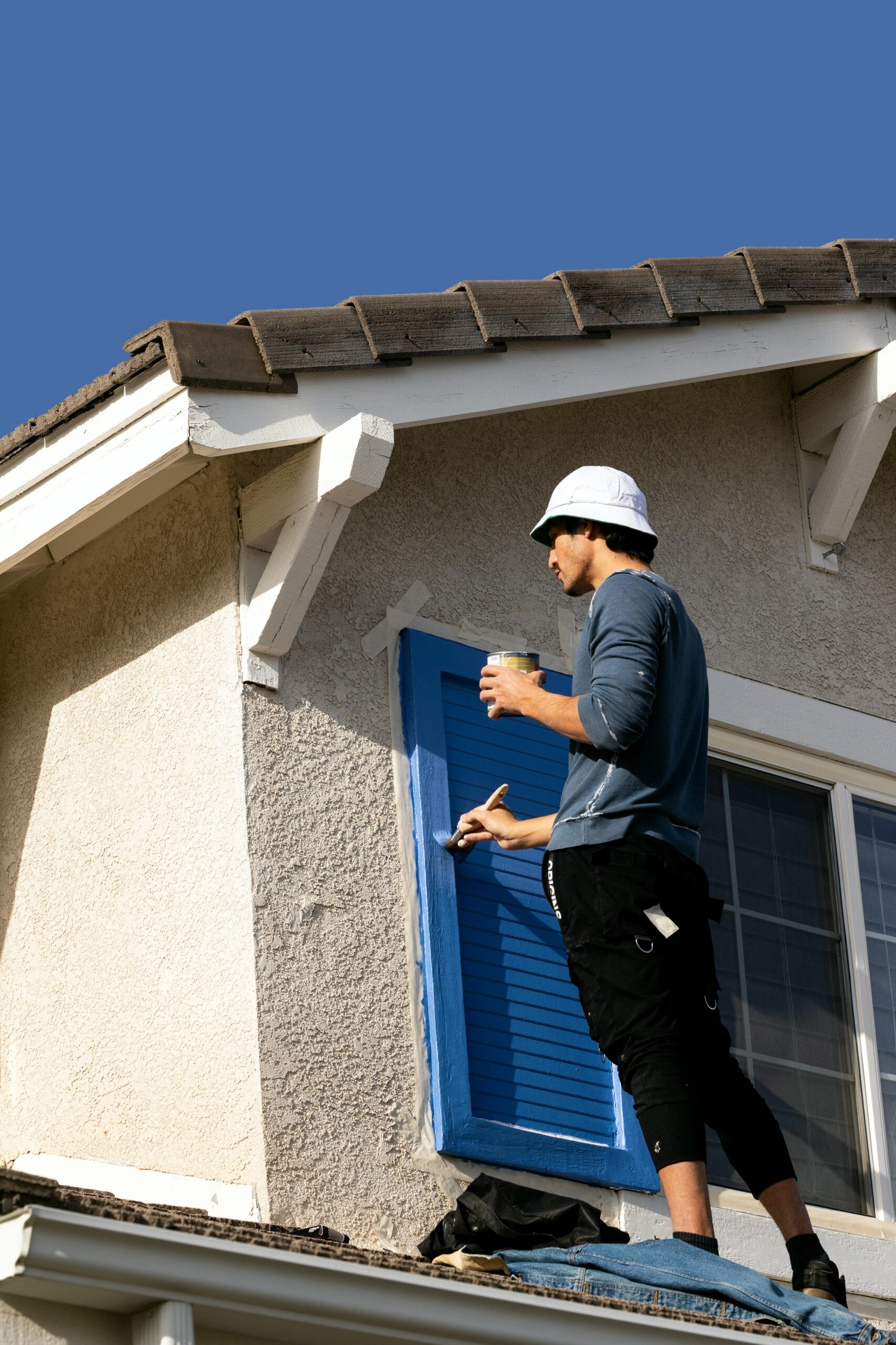 House painter applying blue paint to exterior shutters